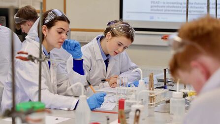 Pupils dresses in white lab coats are making notes as they carry out experiments