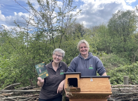 Two Ulster Wildlife staff holding a Let Nature In guide and a hedgehog box