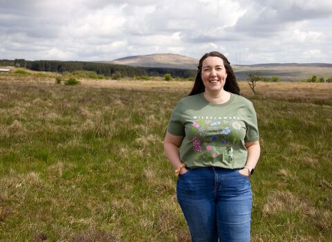 Model wearing Ulster Wildlife women's wildflowers t-shirt in green colour, hands in pockets
